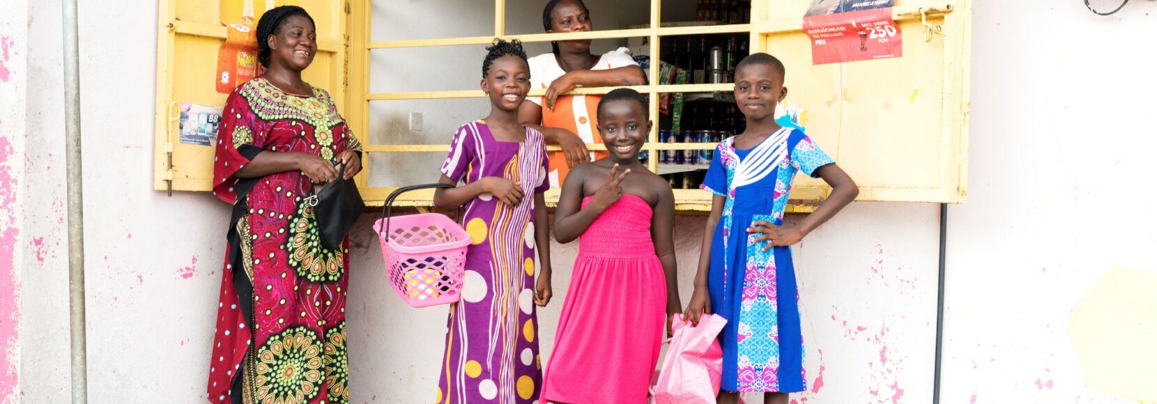 Women and children smile outside a micro-retail shop in Nigeria.