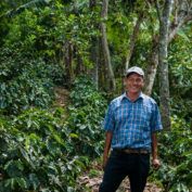 a farmer smiling in front of coffee trees in an example of regenerative agriculture