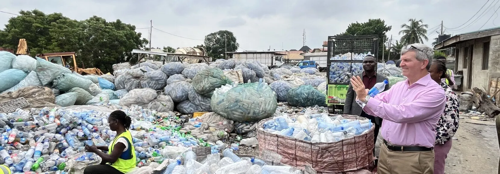 A man in a pink shirt takes a photo of a recycling center in Nigeria.