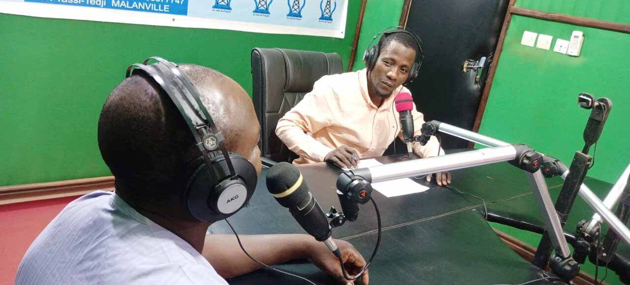 Two men sit in a green room in northern Benin for a radio program.