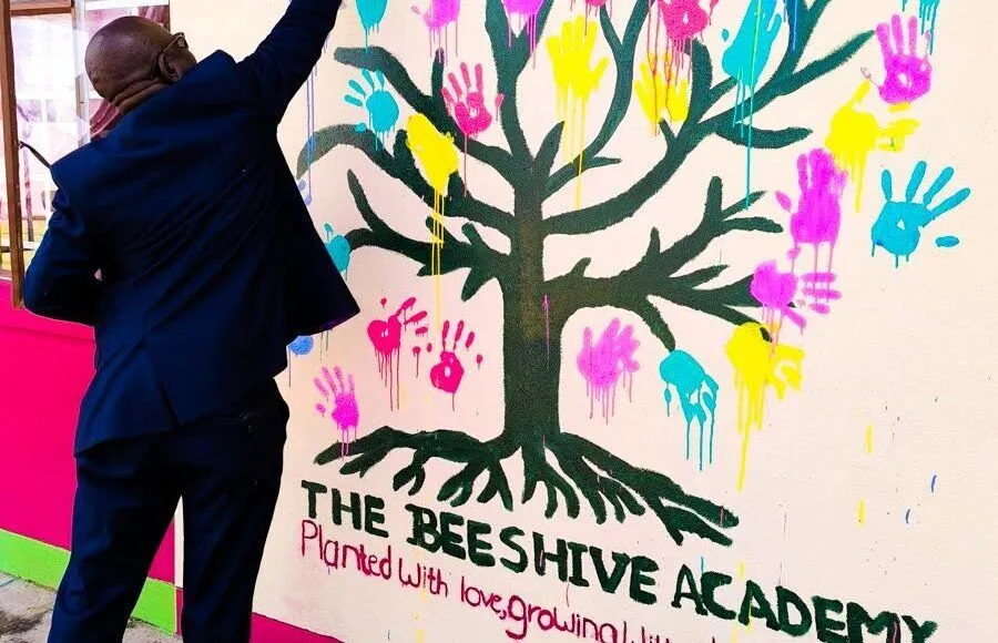 A man reaches his hand out to touch a wall that is filled with painted hands.