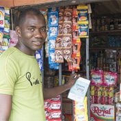 Man smiling in front of a Nigerian mom and pop shop