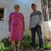 Two people smiling next to pile of bananas