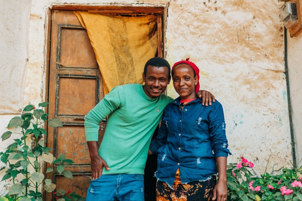The impact of coffee has transformed what life looks like for Lubaba and her son smiling in front of their home