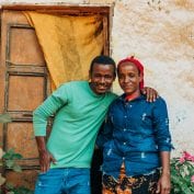 The impact of coffee has transformed what life looks like for Lubaba and her son smiling in front of their home