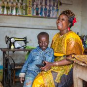 Human-centered design can power incredible solutions for international development. A woman holds a mobile phone near a sewing machine -
