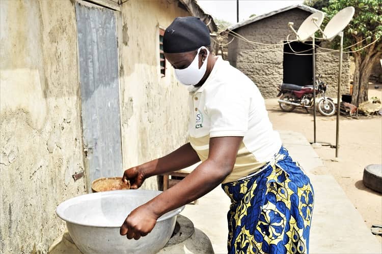 Photo of a woman cashew farmer in Benin wearing a mask and carrying water.