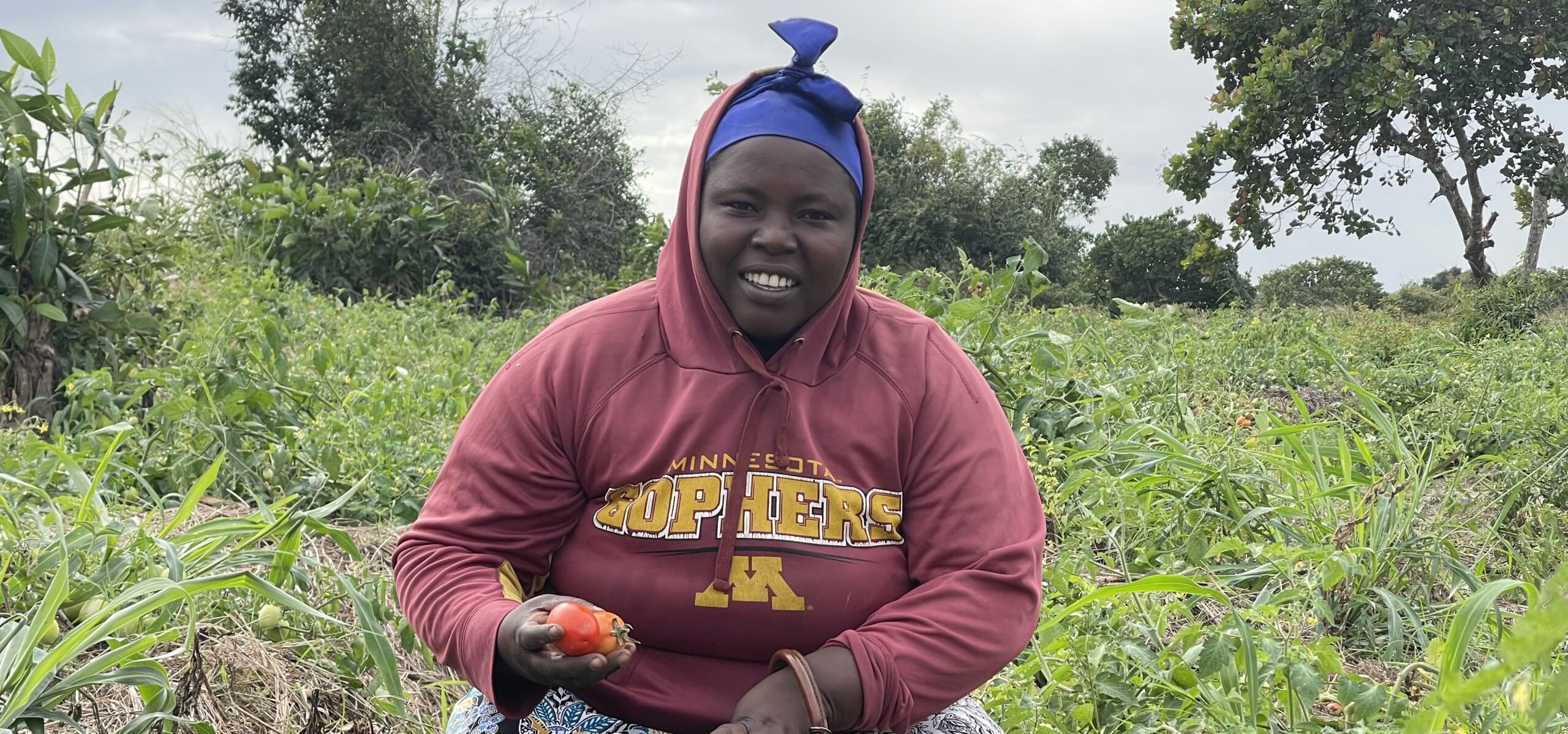 A woman kneels in a field with a bucket of tomatoes.