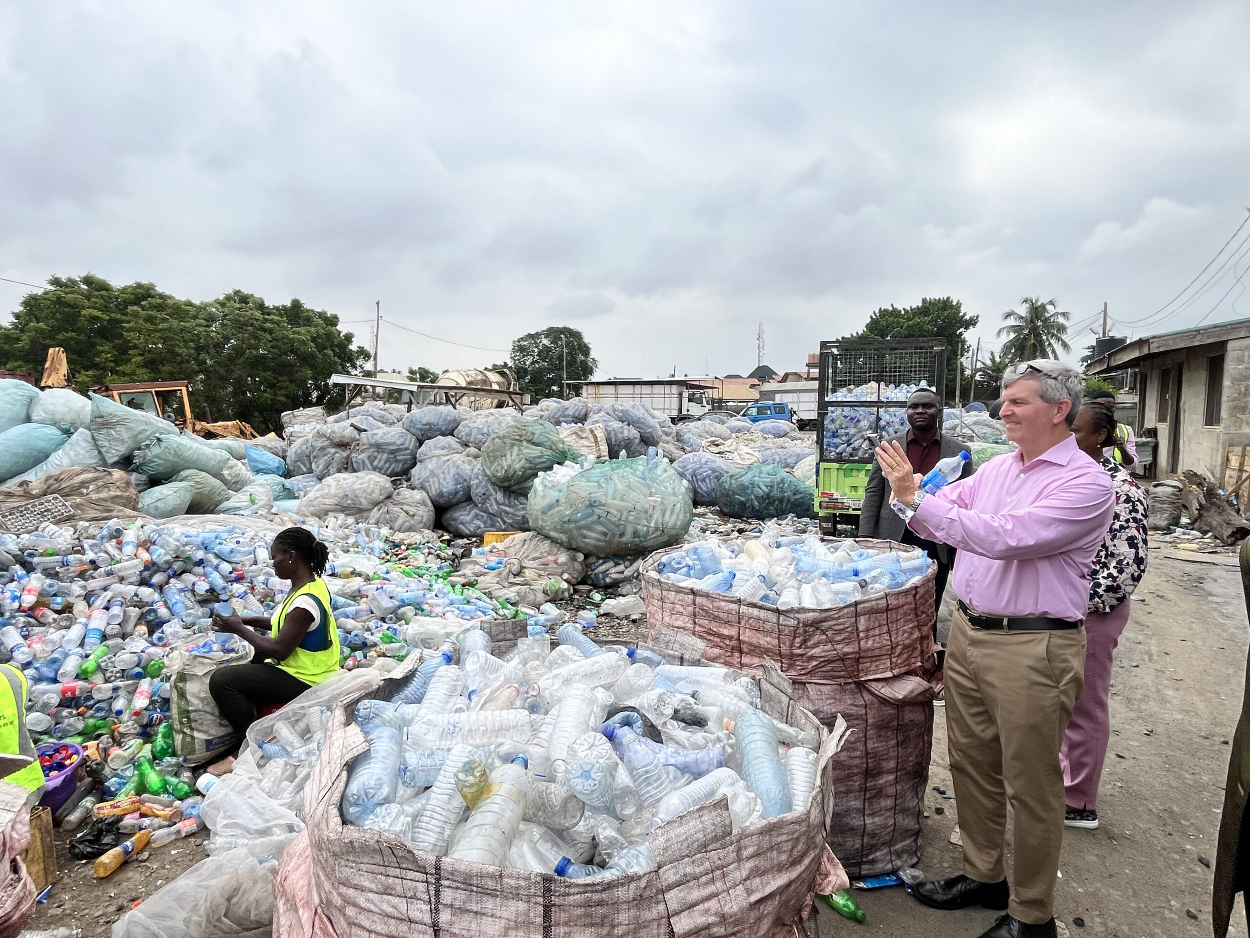 A man in a pink shirt takes a photo of a recycling center in Nigeria.