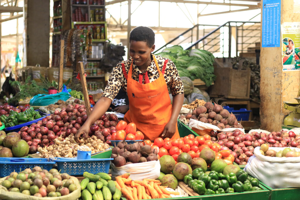 A woman stands and smiles at her fruit and vegetable stand