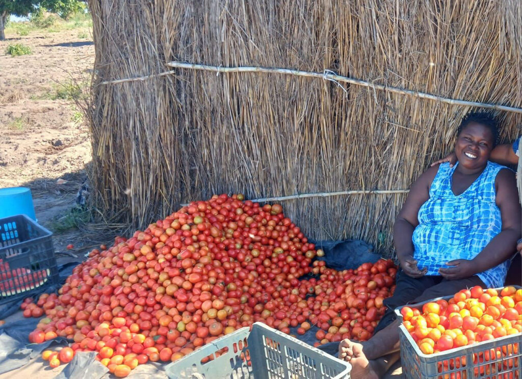 Woman sits smiling next to a pile of tomatoes 