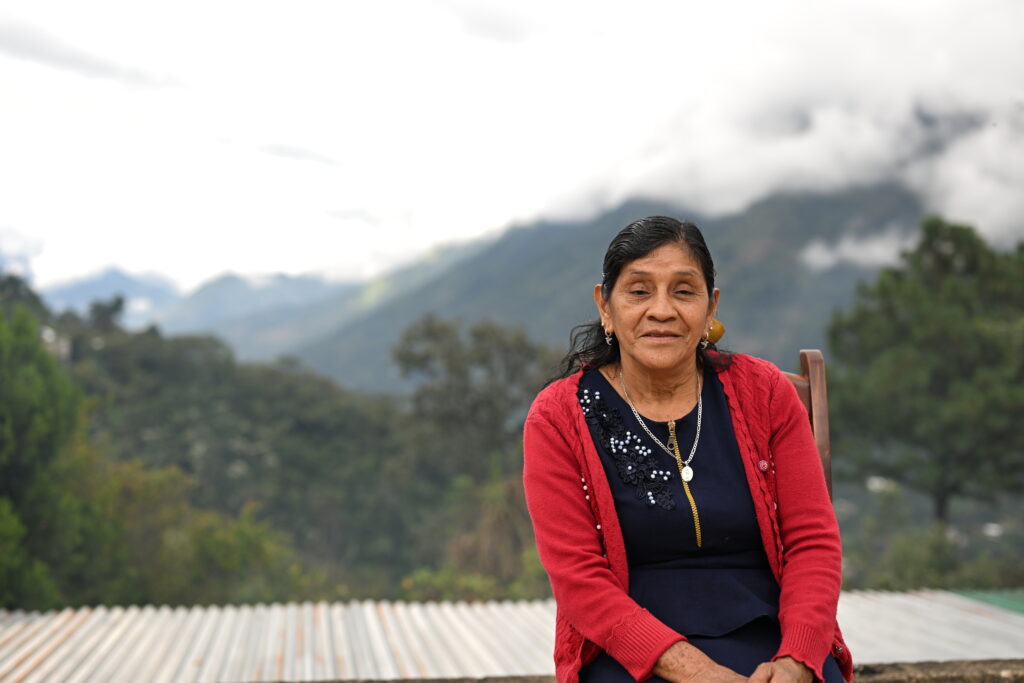 A woman sitting on the rooftop of her home, with mountains in the background