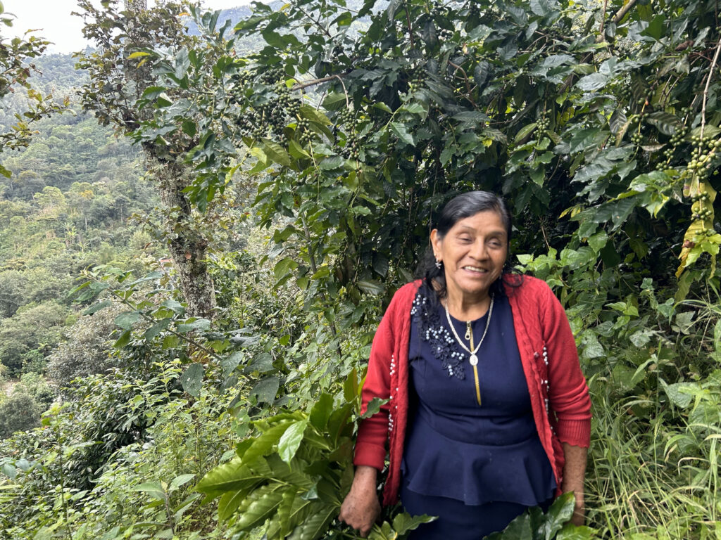 A woman stands smiling in front of her coffee trees