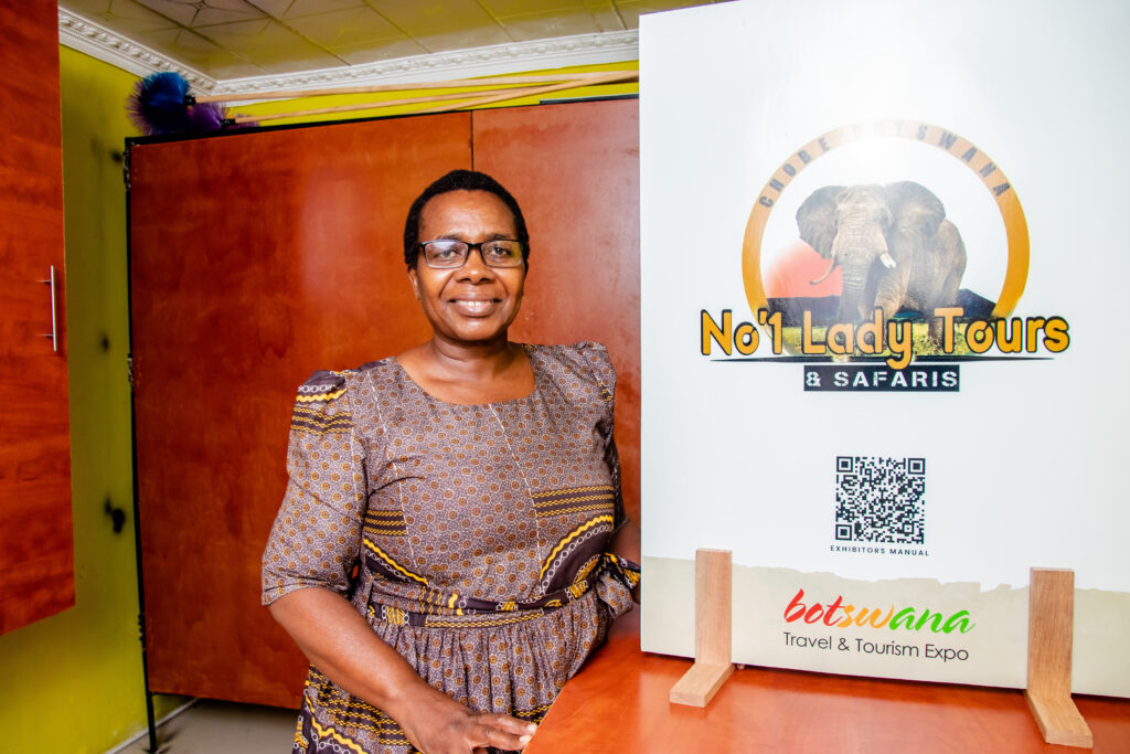 A woman stands in front of a sign for her business in Botswana. 