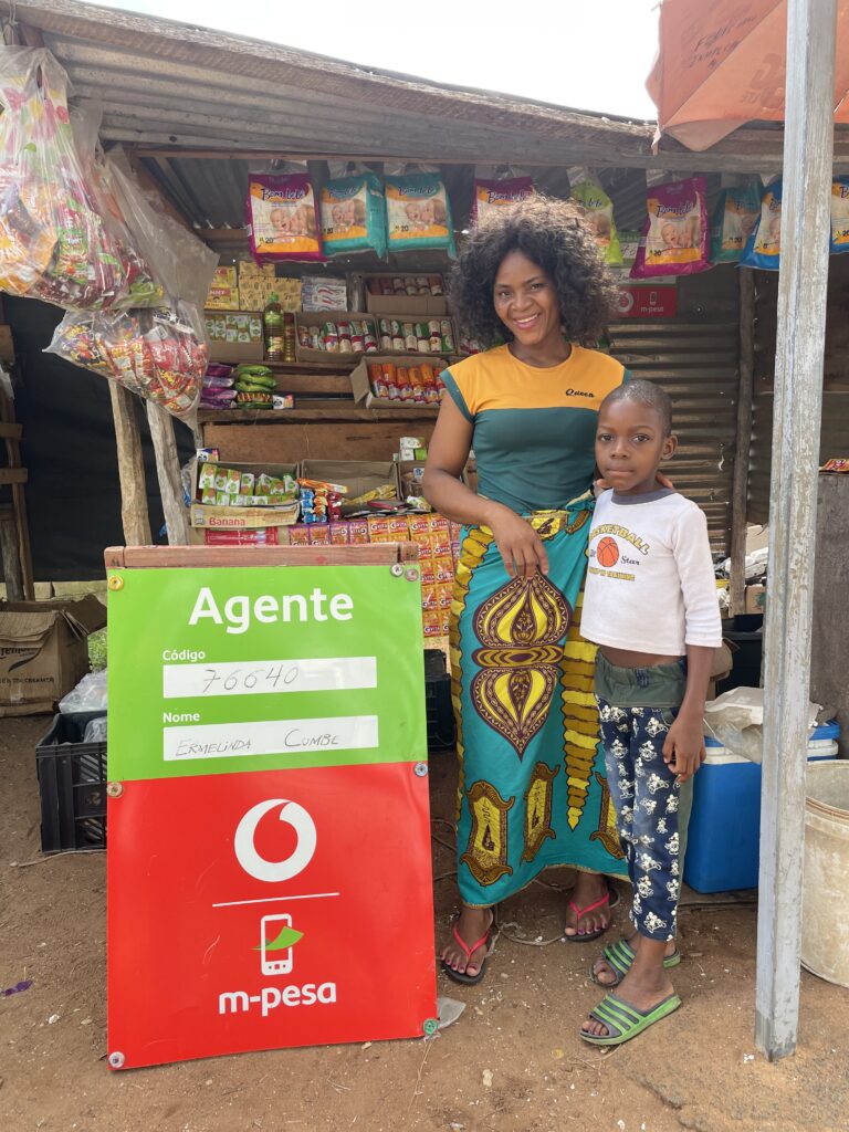 A young entrepreneur in Mozambique stands in her grocery store with her daughter. With support from TechnoServe, she learned how to grow her business and achieve business solutions to poverty.