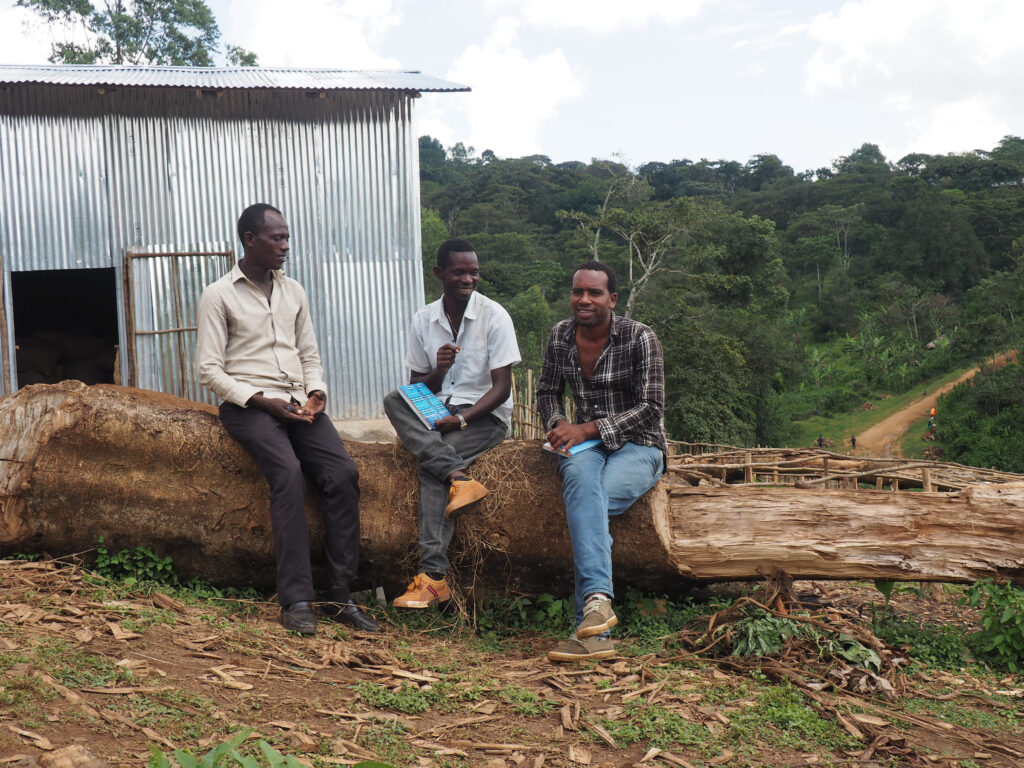 Three men sit on a log in front of a forest in Ethiopia