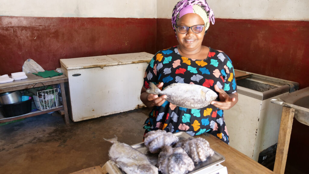 A woman proudly holding up a whole fish and smiling.