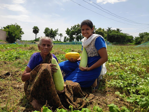 Archana Stalin (right) sits with another woman farmer holding vegetables in a green field. She learned important business skills to help her startup succeed. 
