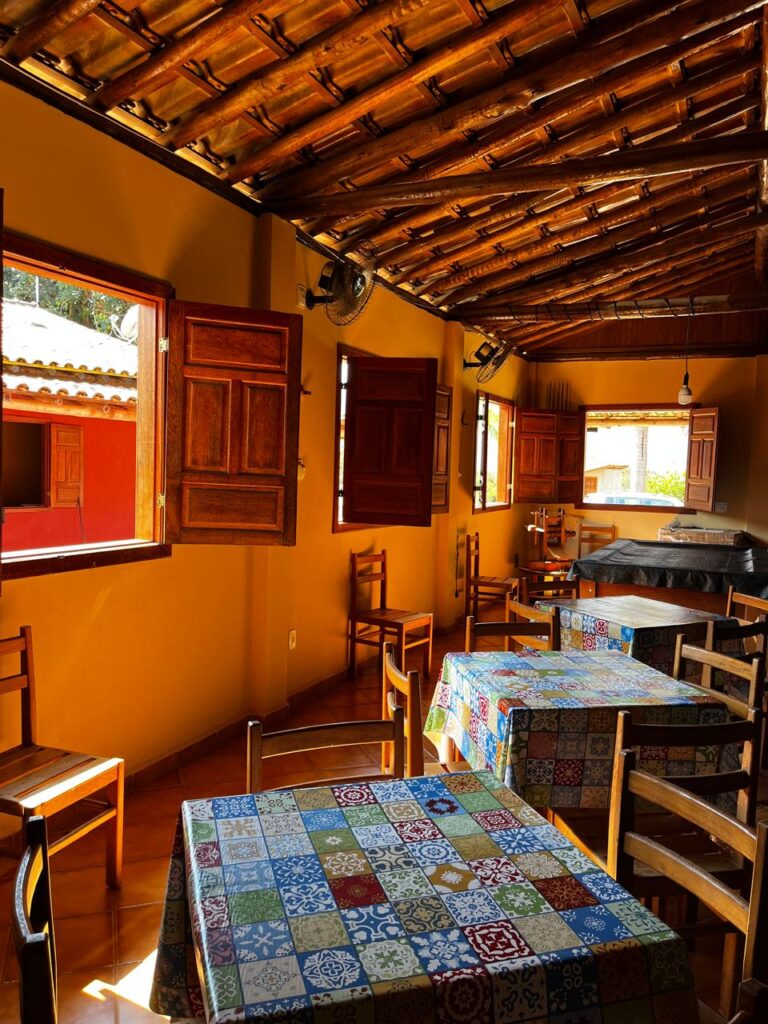 A restaurant with open windows and tables with checkered table clothes and wooden chairs.