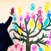 A man reaches his hand out to touch a wall that is filled with painted hands.