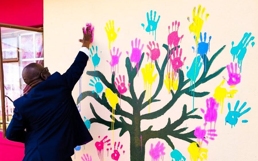 A man reaches his hand out to touch a wall that is filled with painted hands.